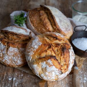 Small-batch sourdough loaf on rustic wooden table with linen cloth